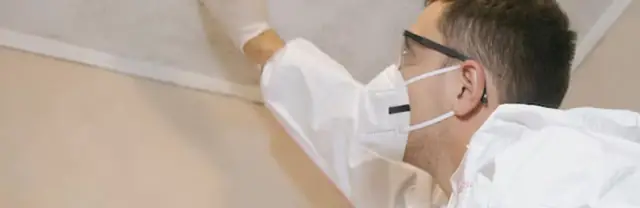 Person in a mask and gloves wiping a ceiling edge