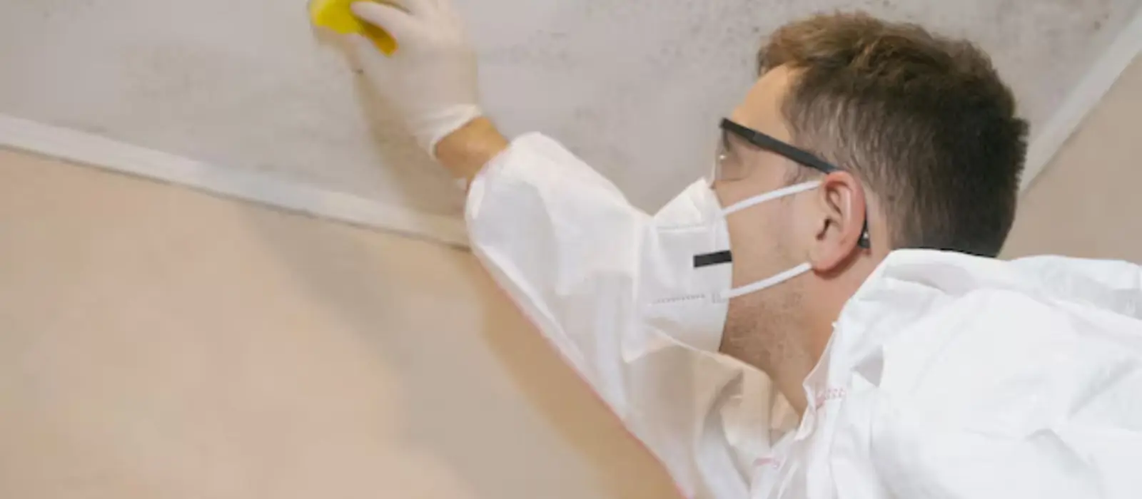 Person in a mask and gloves wiping a ceiling edge
